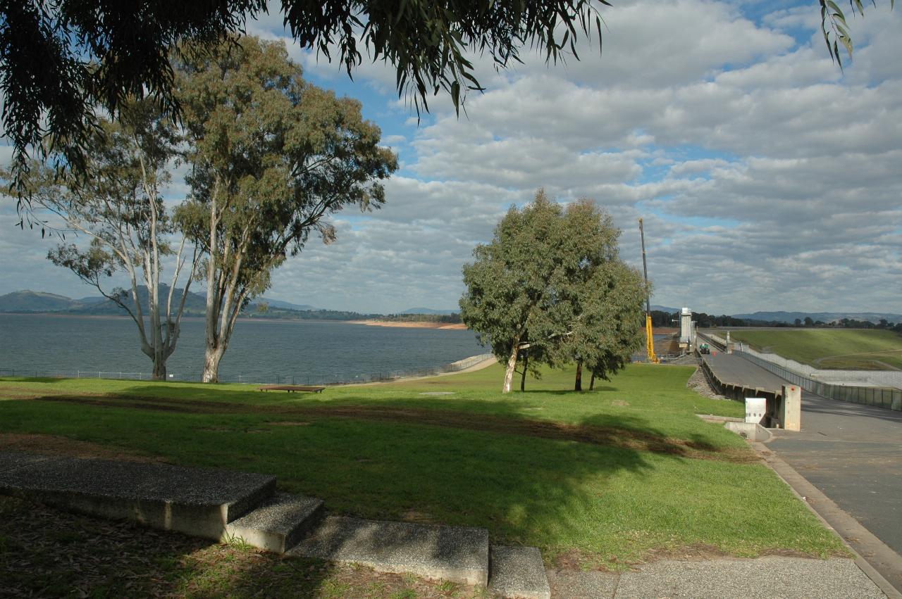 Grassy area, with trees, lake behind, distant hills, and dam wall on right