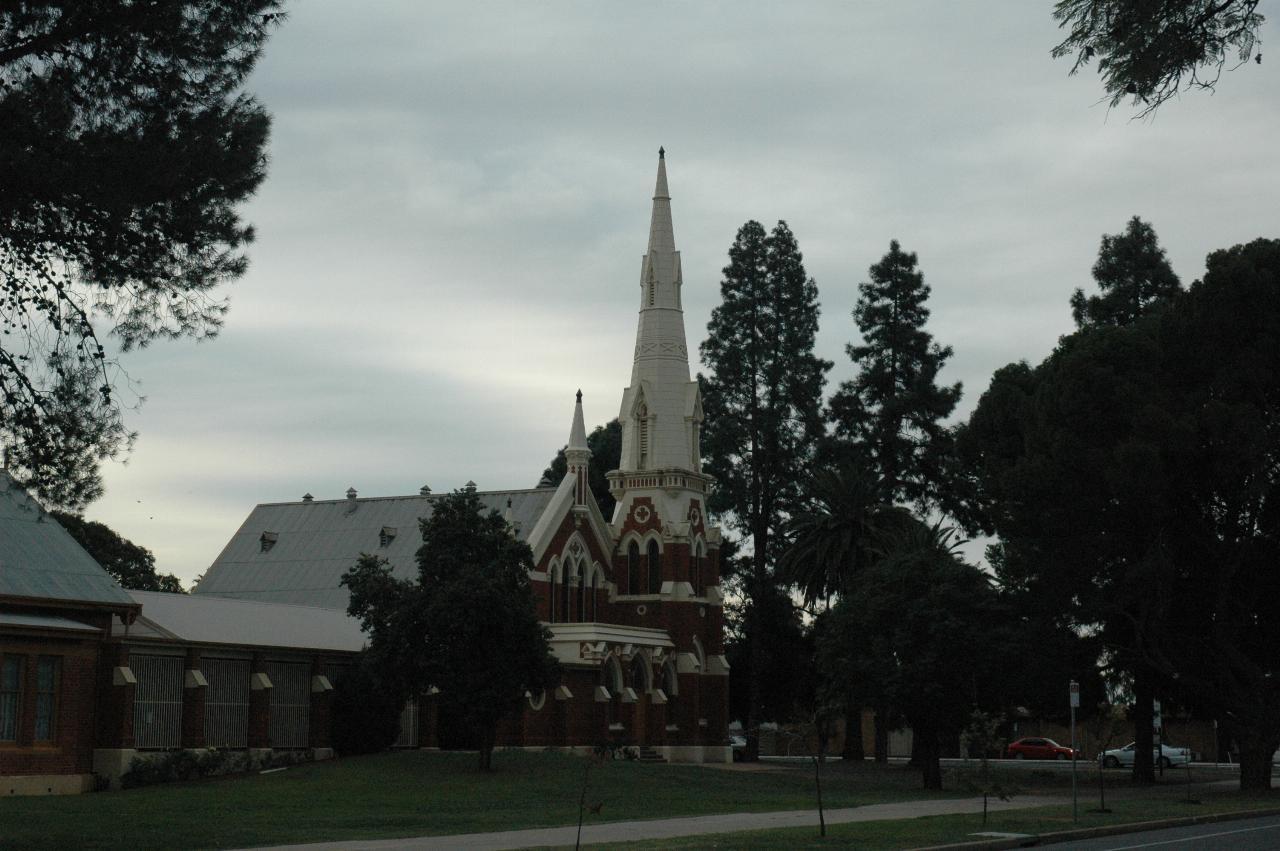 Dark brick church, with white trim and very tall spire, also white, trees behind