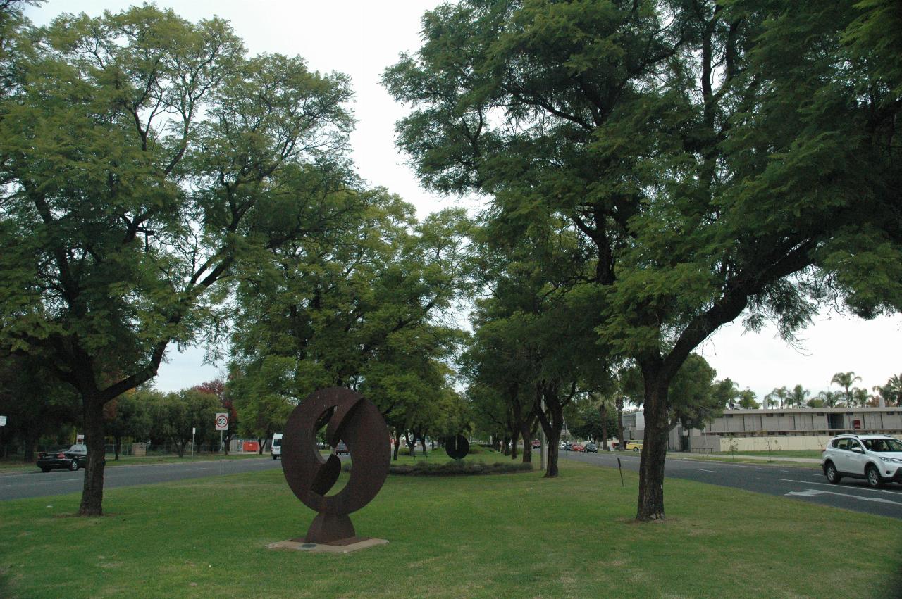 Looking along wide median strip with trees and a sculpture something like the Ying & Yang diagram