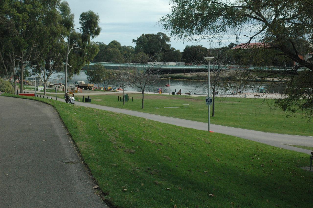 Grassy bank with several paths, river and pedestrian bridge across water