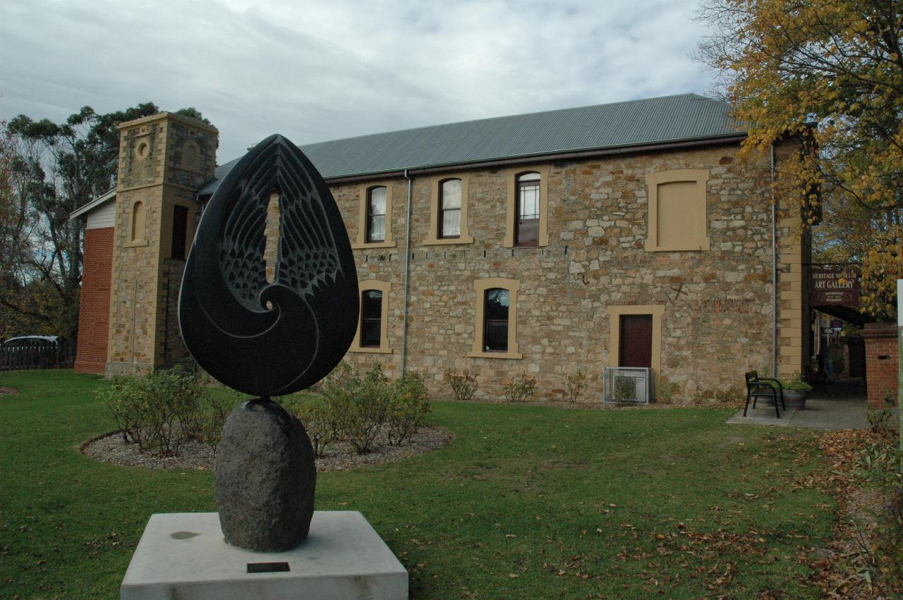 Two storey stone building with small tower, modest garden and black tear drop sculpture on stone support