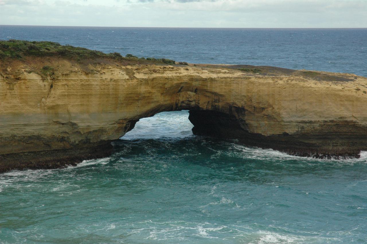 Ochre coloured cliffs on island with ocean level tunnel in the middle