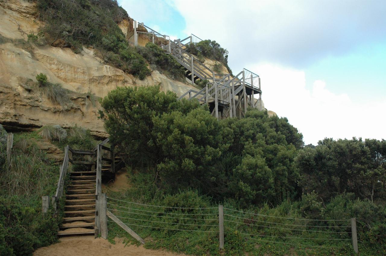 Wooden stairs up the side of ochre coloured cliff, and shrubs at the sandy bottom
