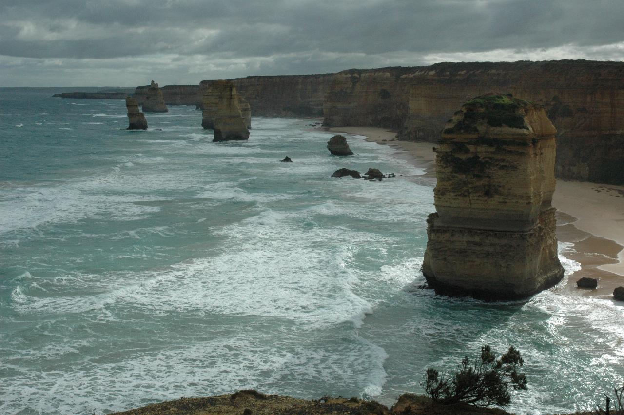 Tall coastal, ochre coloured cliffs with beach and waves, and varied shaped stacks in the ocean
