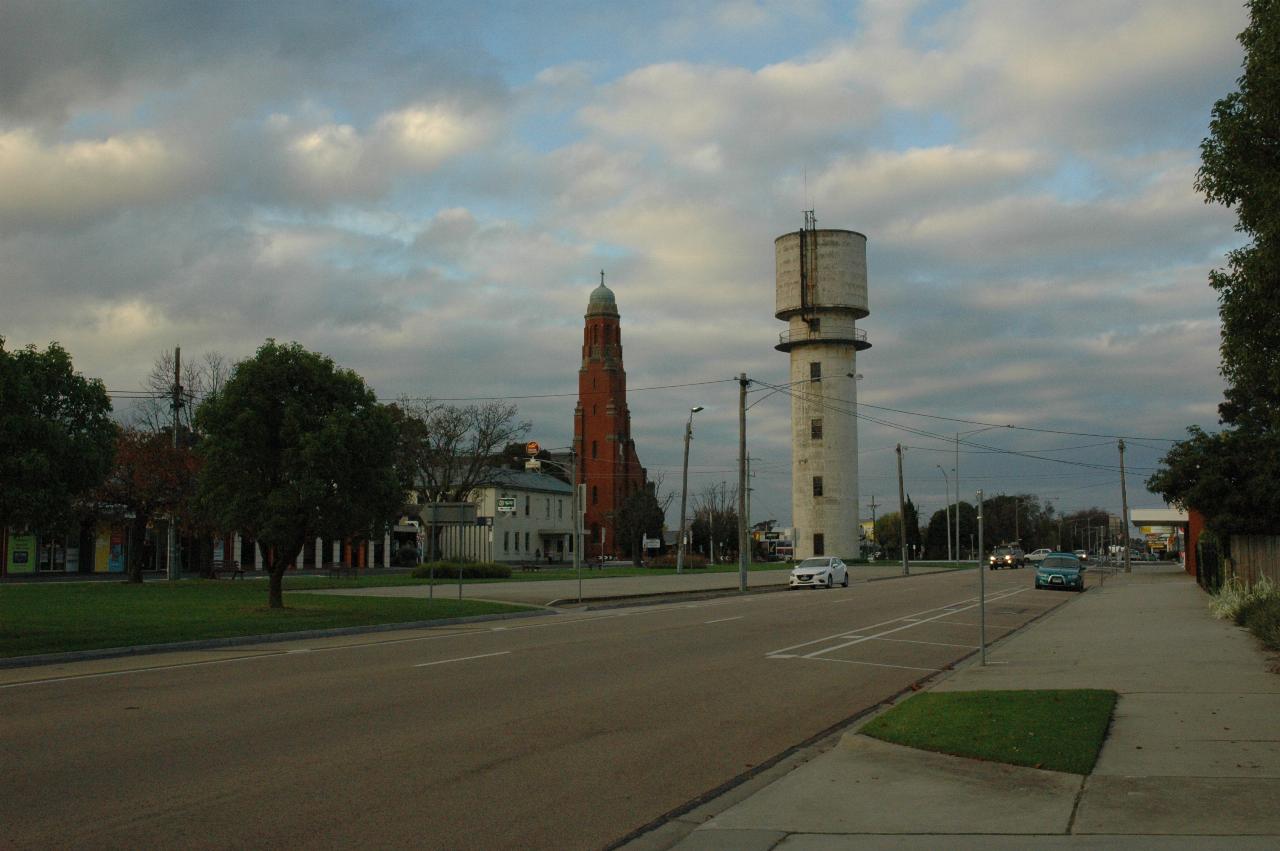Cement cylindrical water tower in median strip, in front of church with tall spire