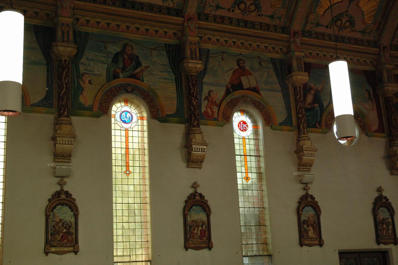 Wall with tall, thin windows, murals above and along wall for Stations of the Cross