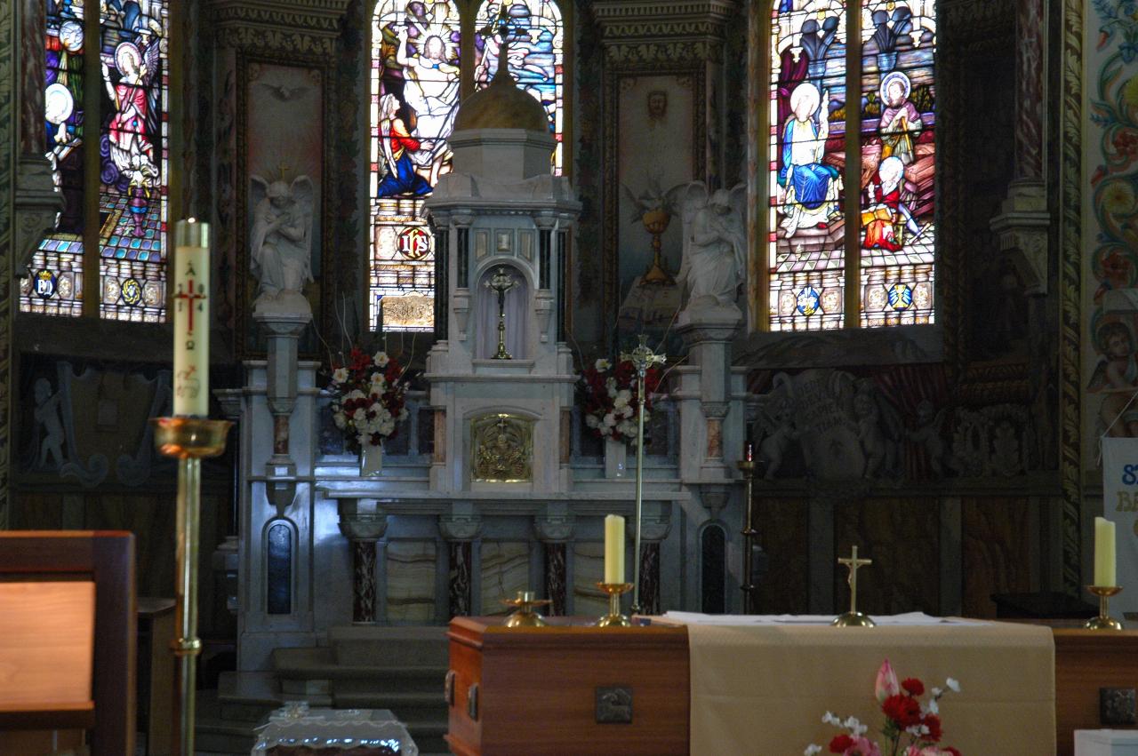 Old marble altar at back of church with stained glass windows beside it, new altar partly visible in front