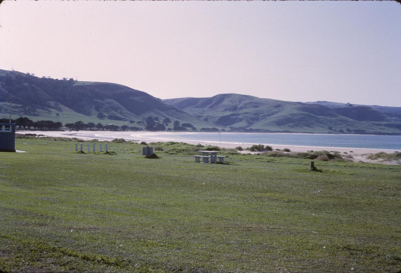 Across picnic area, beach, bay towards rounded green hills