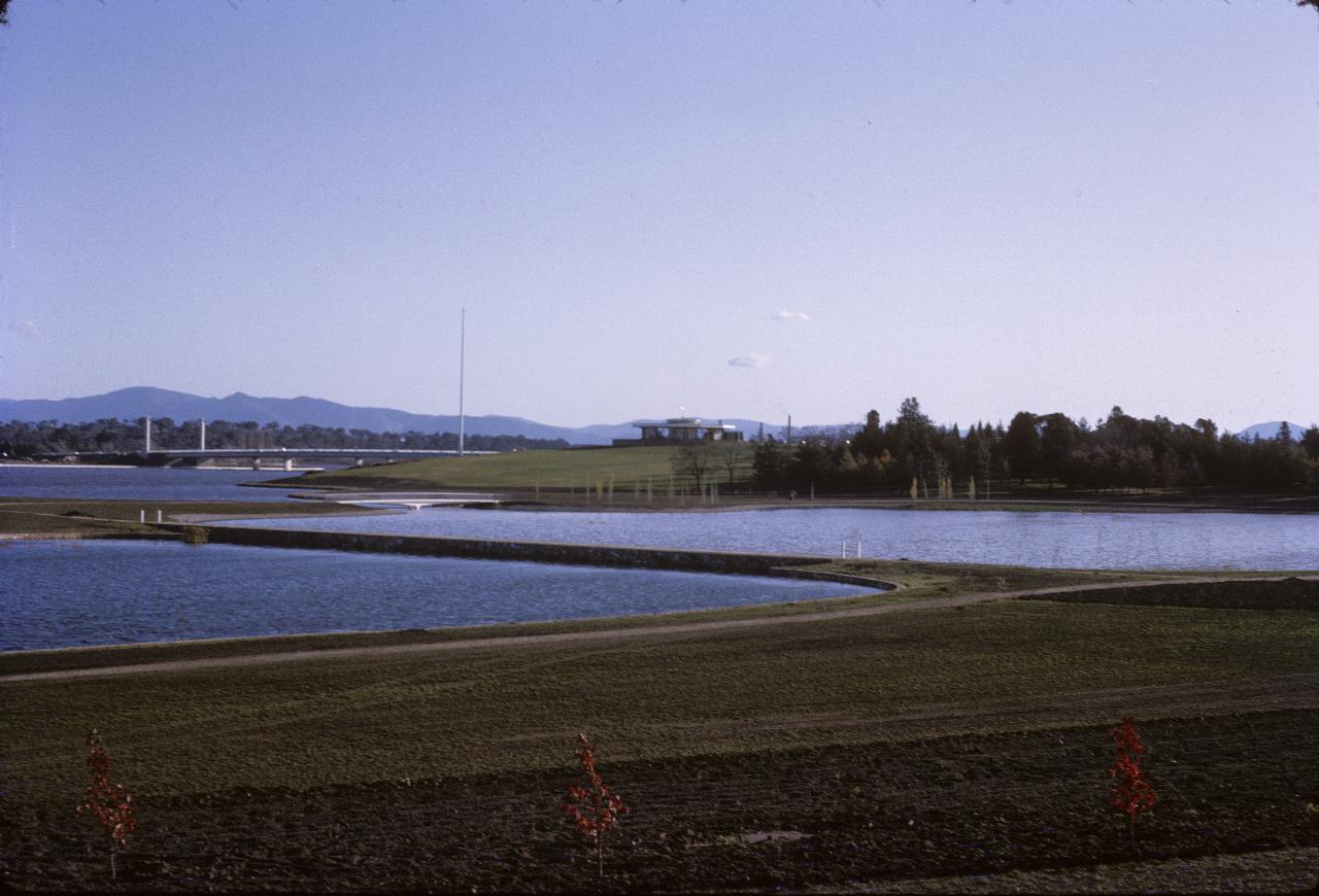 Planted grounds, ponds and bridges across lake in distance