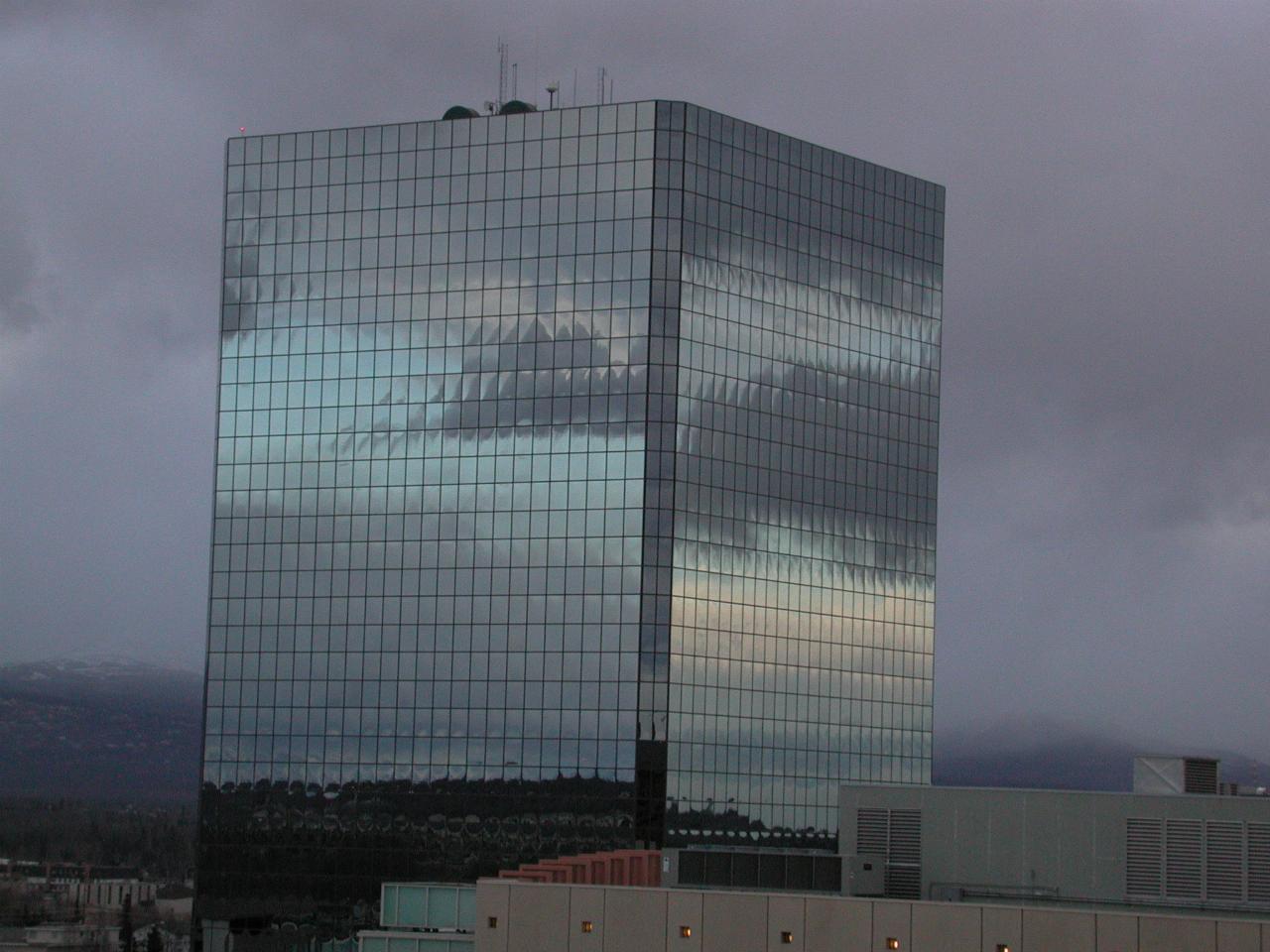 A glass office building in Anchorage reflects the sky and clouds