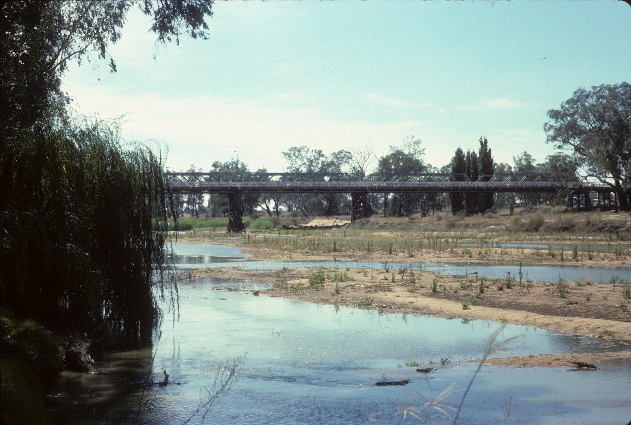 Long wooden bridge over shallow, wide, mostly dry river
