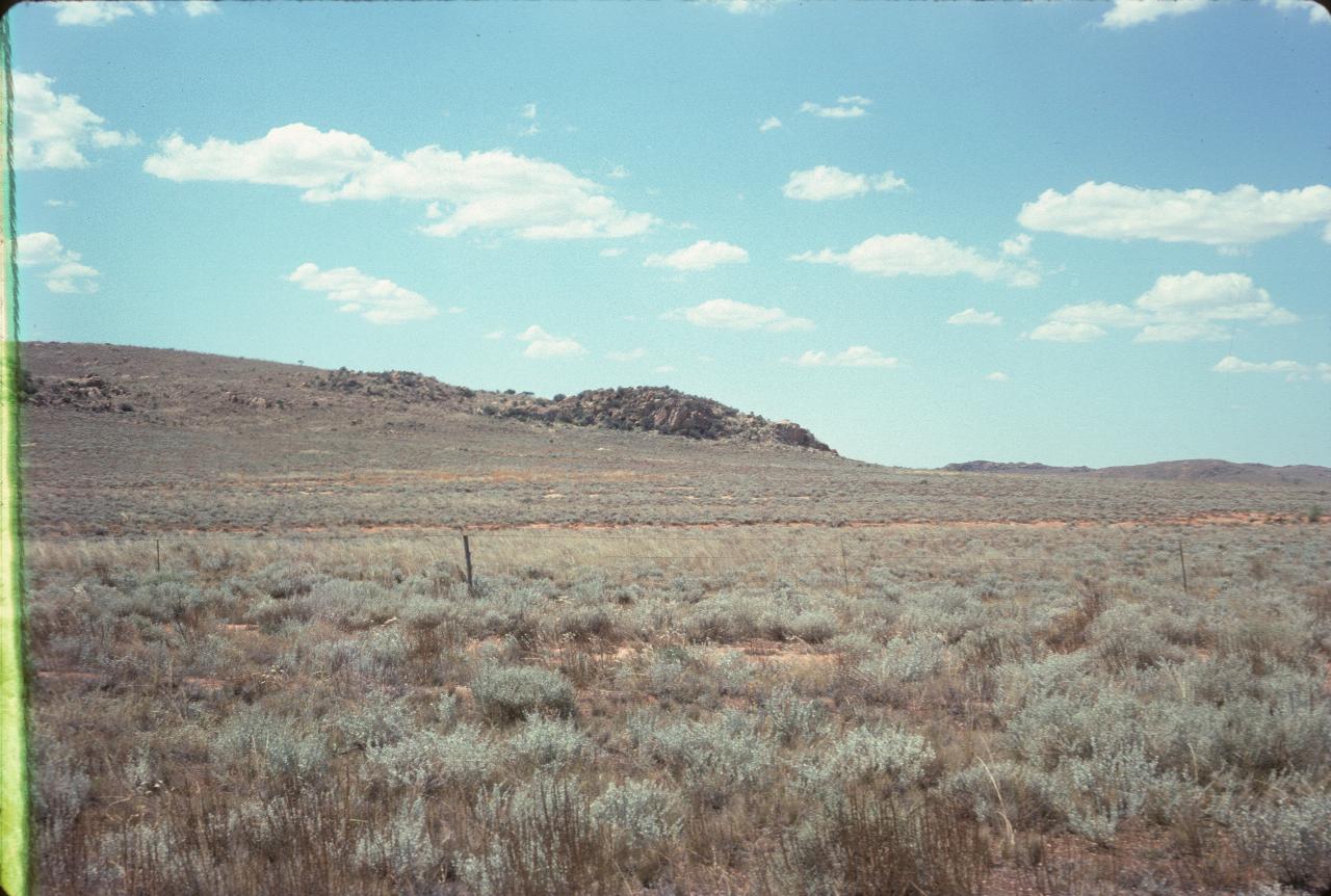 Gentle hill with rocky outcrop; low vegetation on dry ground
