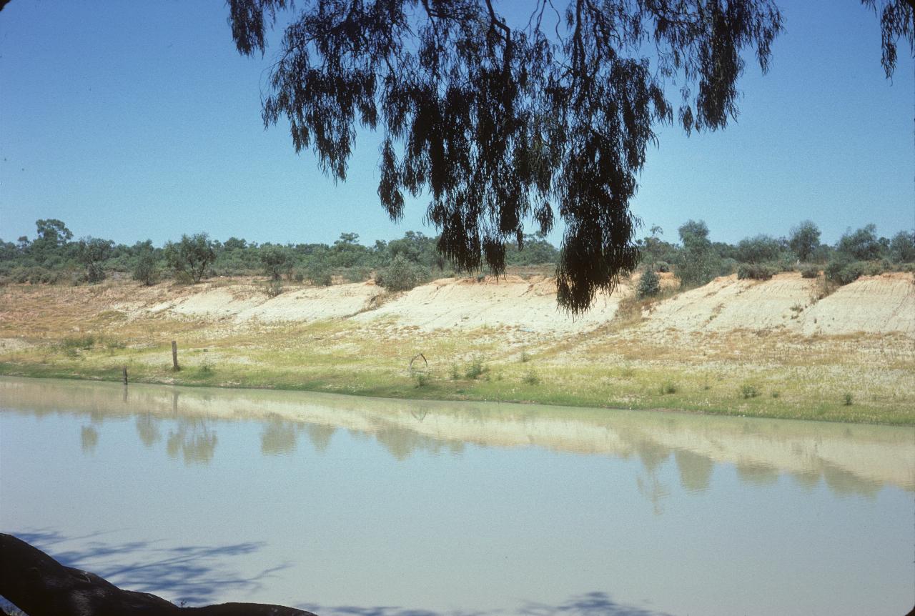 Tan coloured river below gentle banks, low vegetation above