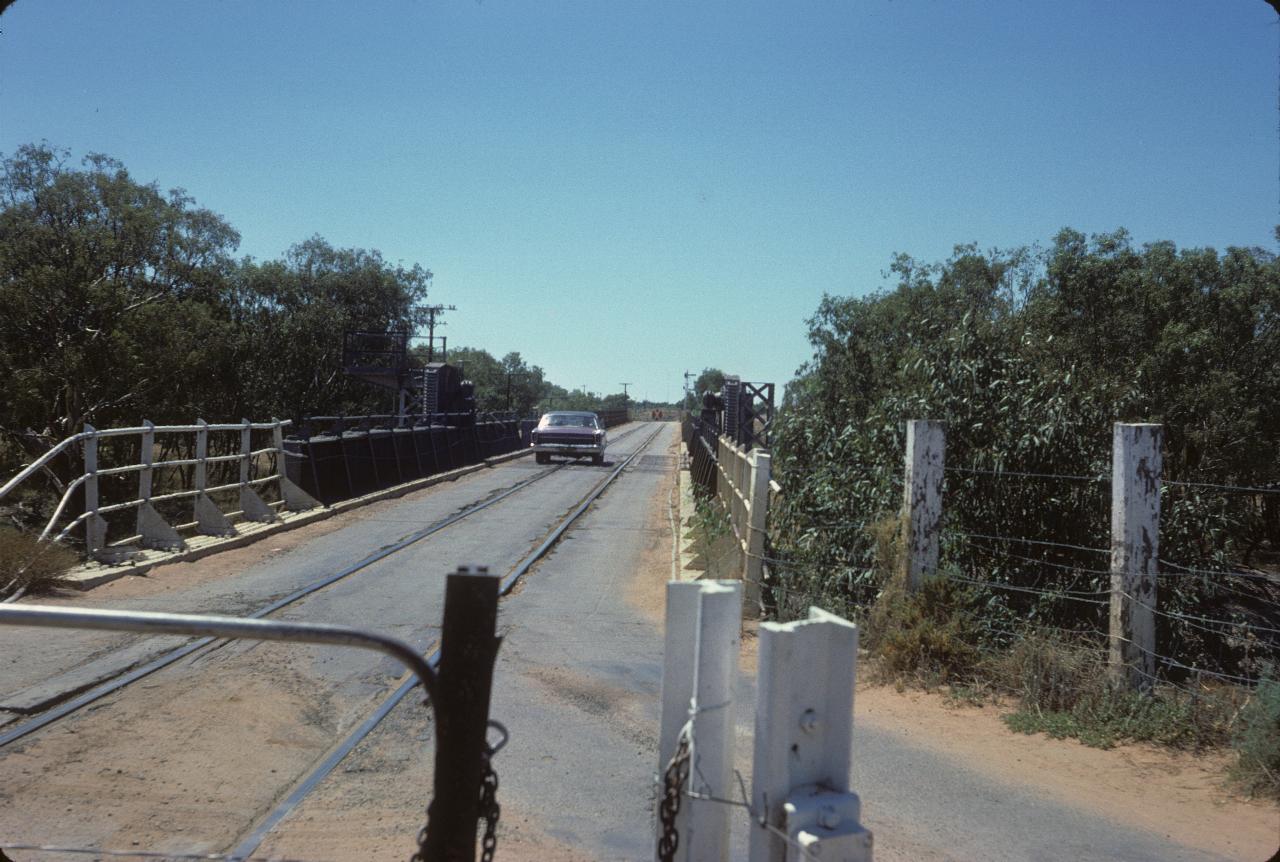 Car on single lane bridge with rail line down middle