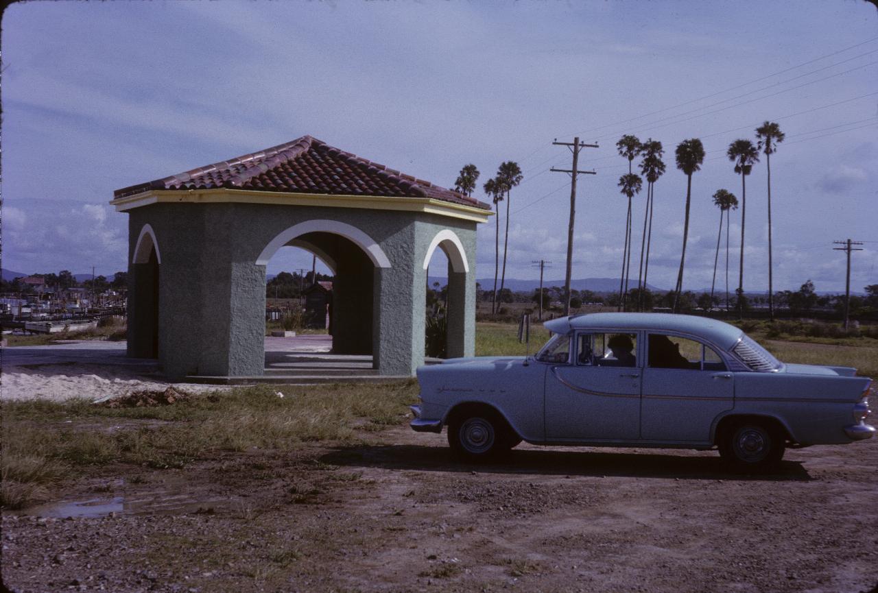 Hexagonal pavillion with green walls, red tile roof, adjacent to blue car