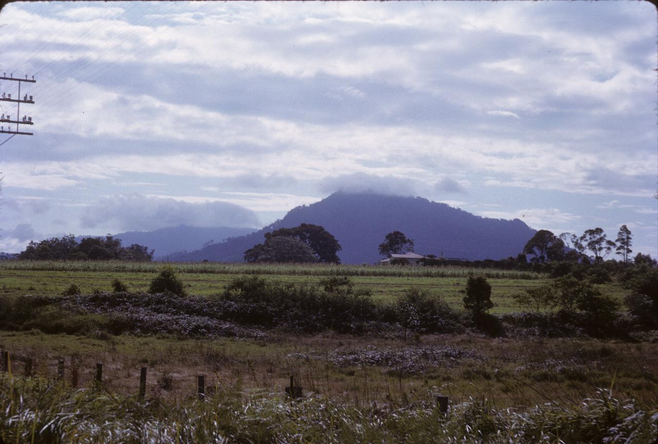 Green fields, partly harvested, leading to hills with cloud covered top