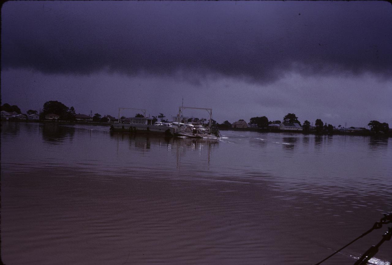 Ferry with cars crossing river under dark cloud