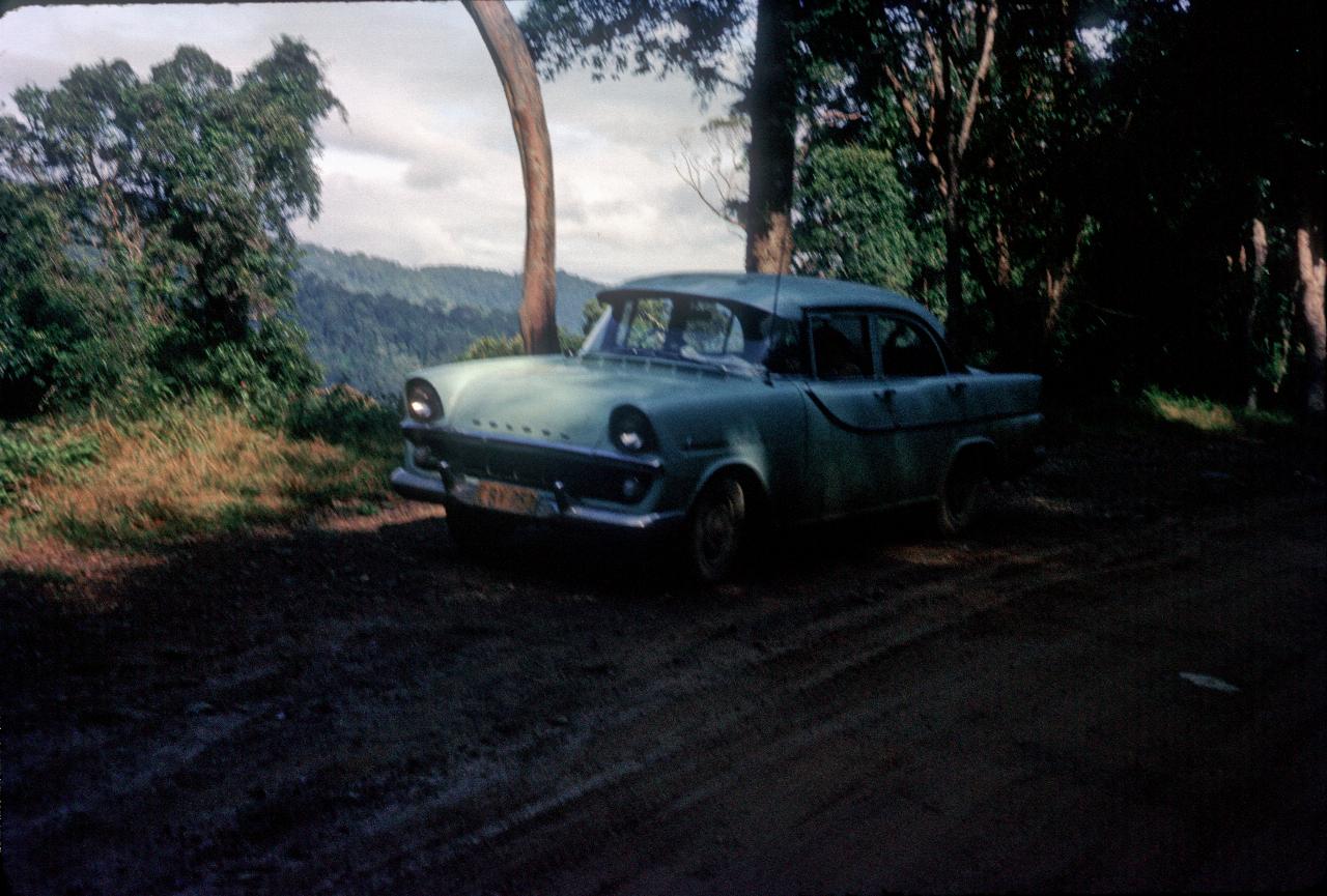 Blue car parked beside muddy road on edge of mountain