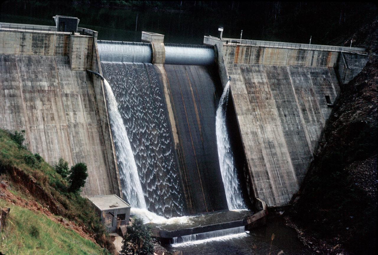 Concrete dam with water flowing over spillway in centre