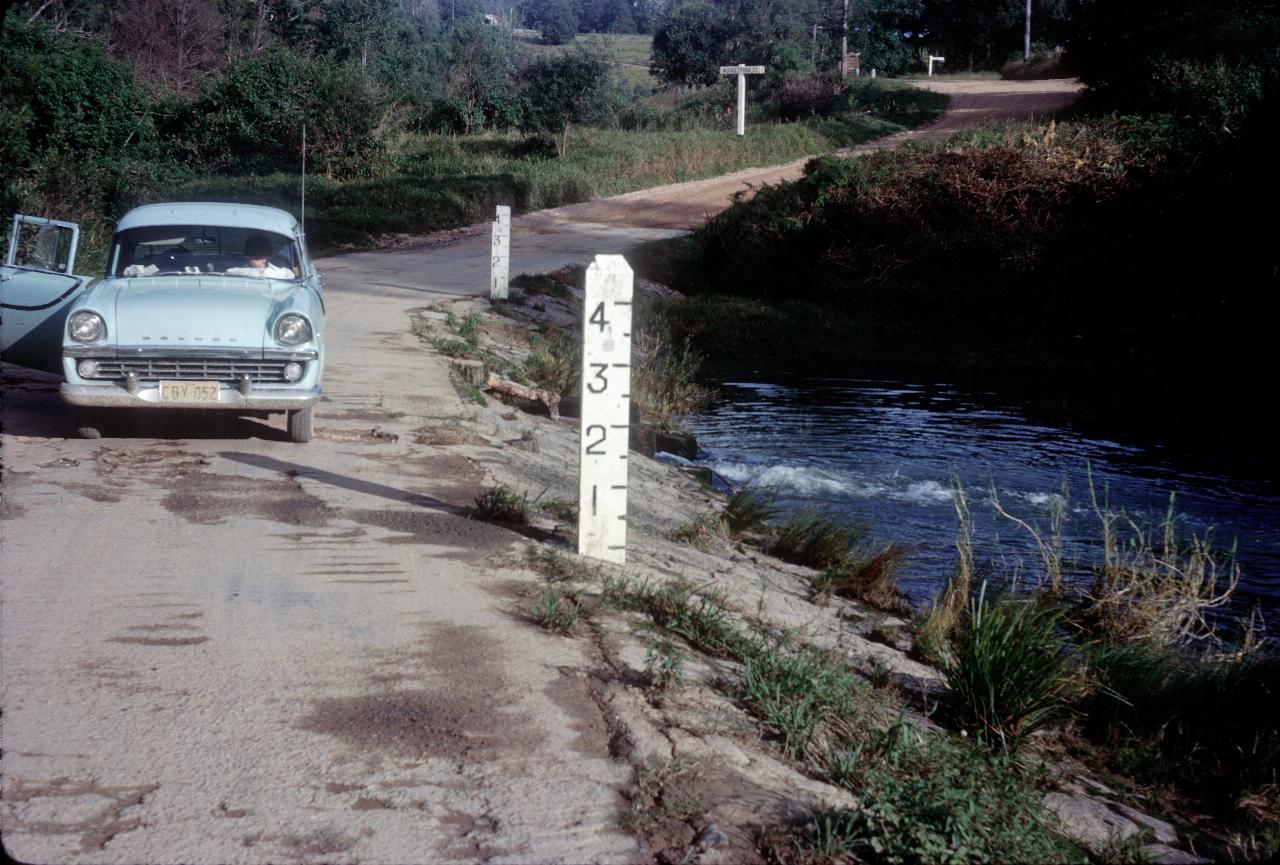 Blue car stopped on causeway beside 4 foot high flood marker