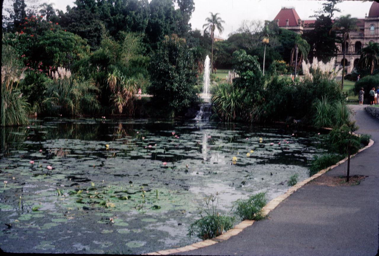 Lily pond with fountain behind and old stone building with red roof behind