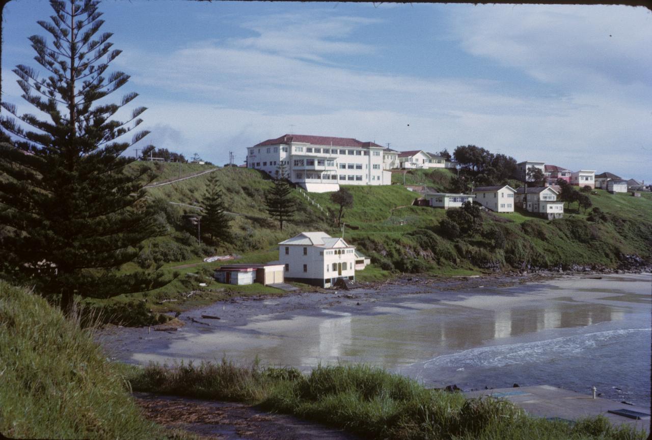 White building on ridge overlooking white surf club house on beach