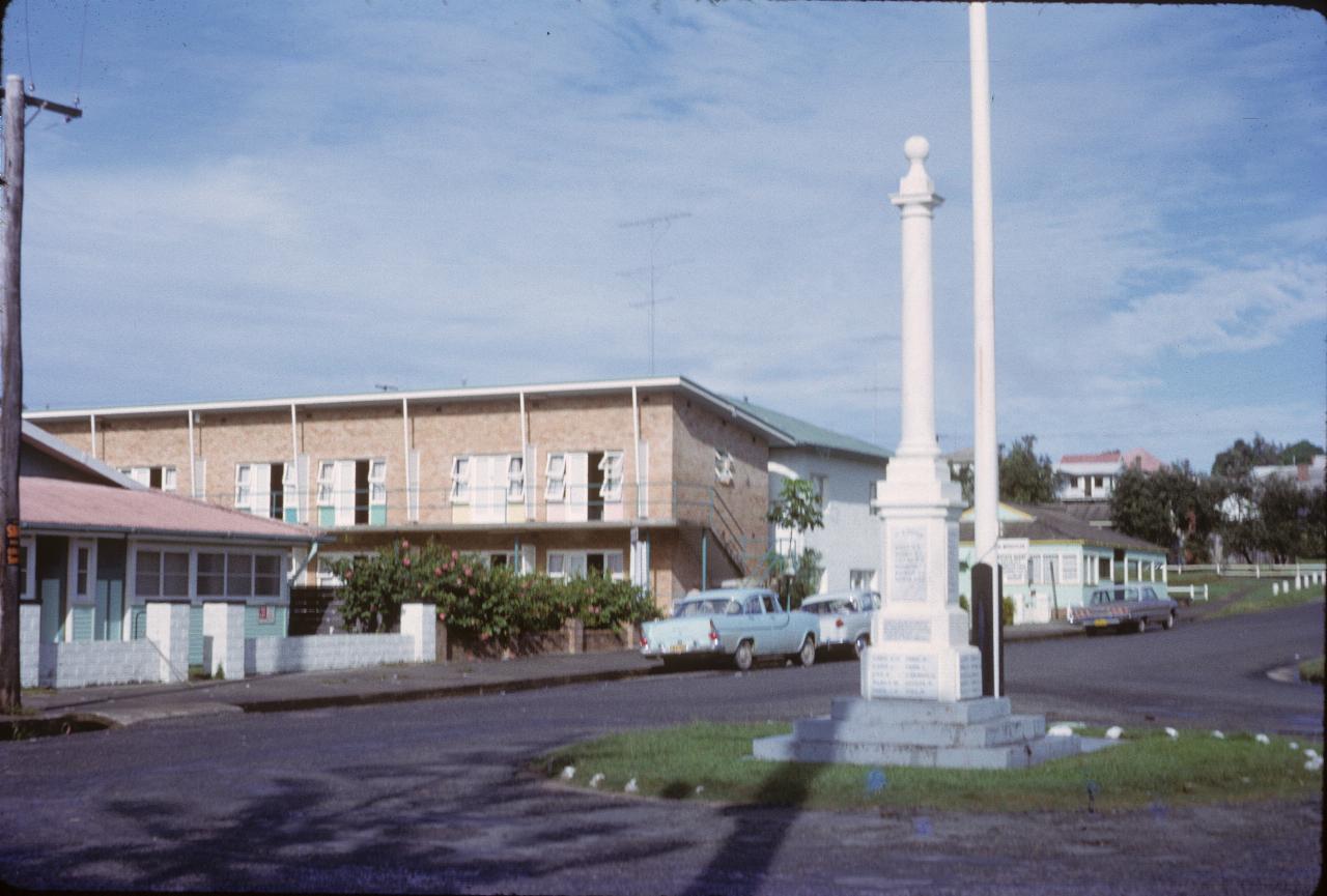 Two storey brick building with sloping roof; white column on plinth in foreground