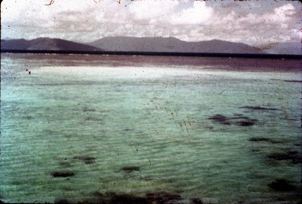 Light coloured sea, to small breaking waves then dark sea to mainland mountains in distance