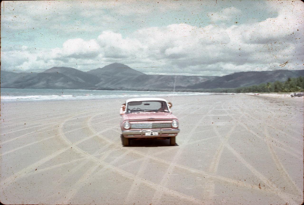 Car on sandy beach; ocean to the left, mountains in rear