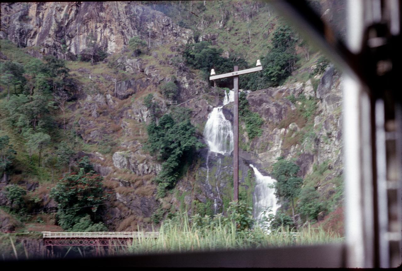 View from train of waterfall over very steep rocks and under train bridge