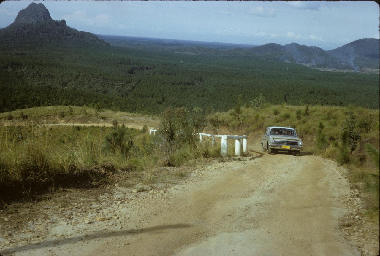 Car driving up dirt road and a volcanic plug and forest in background