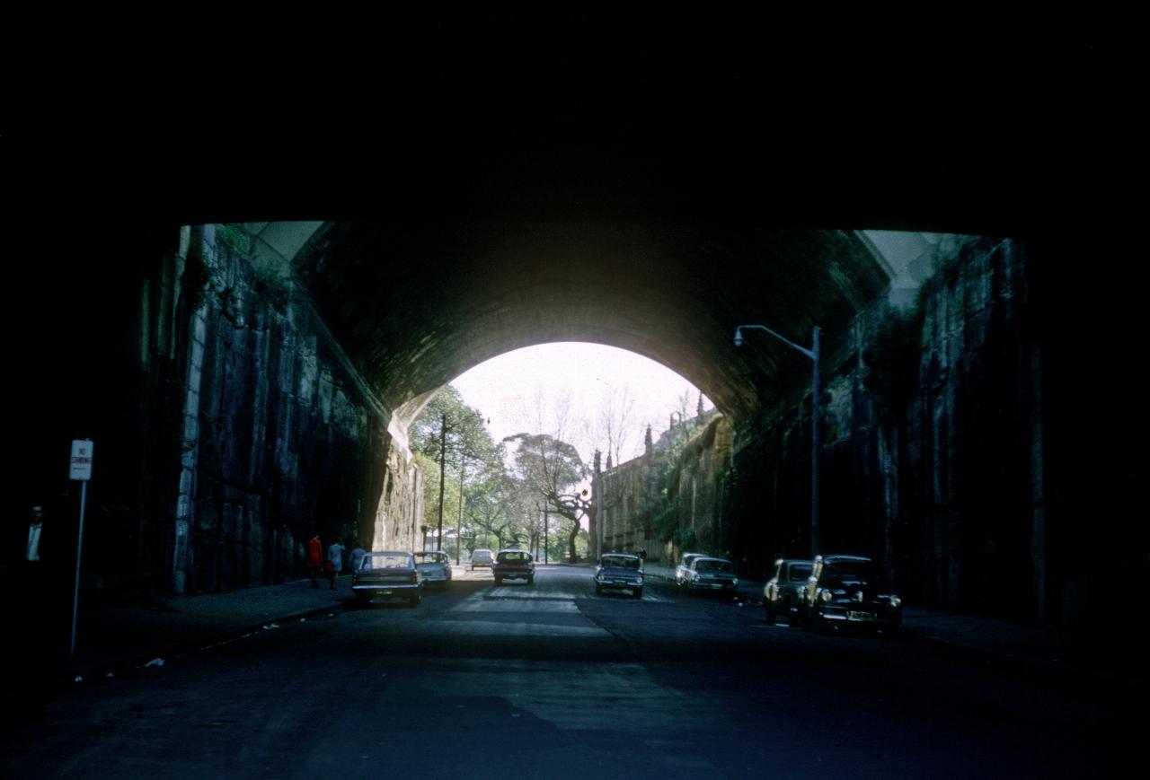 Rock cutting with bridges over it, and cars parked on road