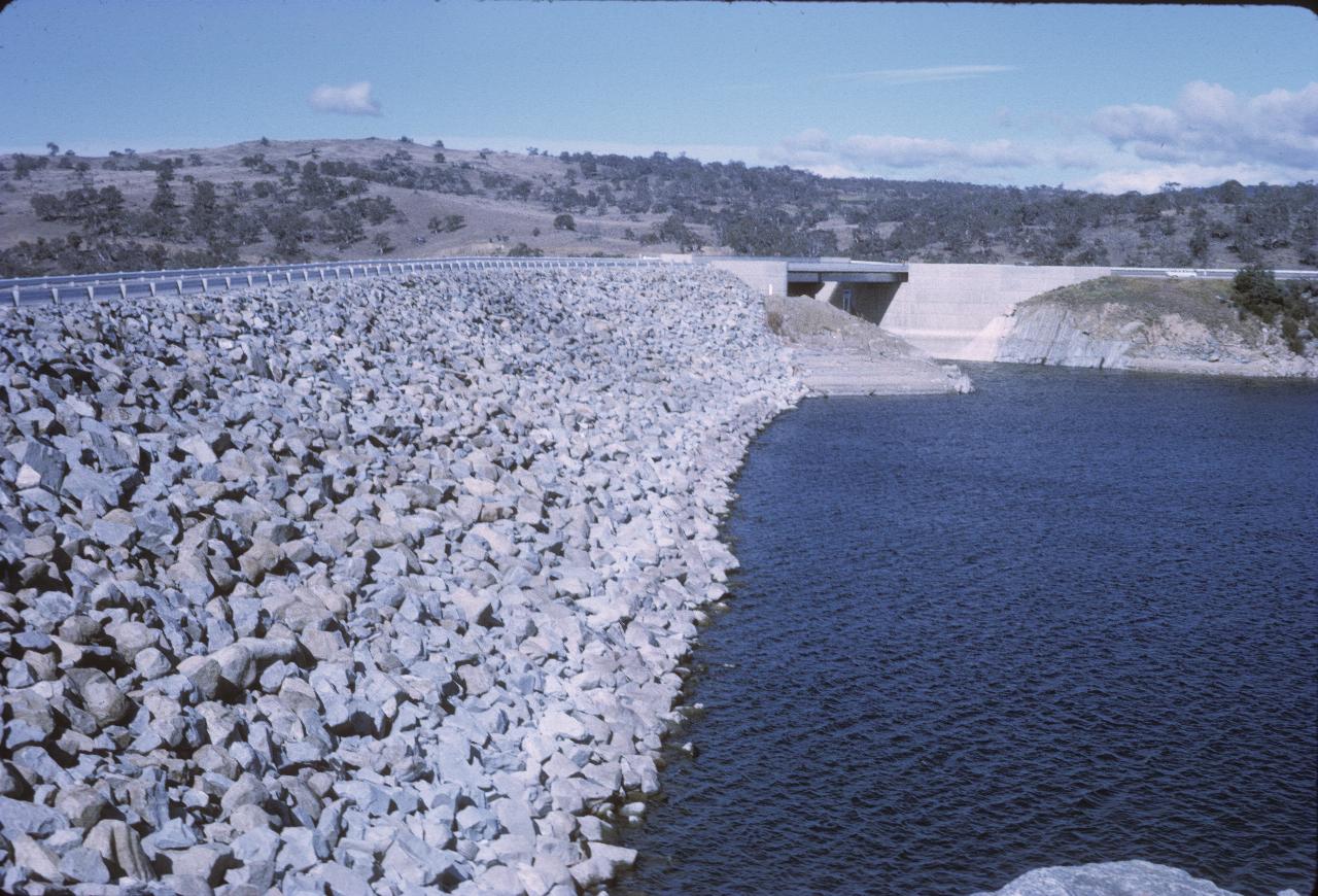 Rock covered dam wall, with road on top and cement spillway at far end