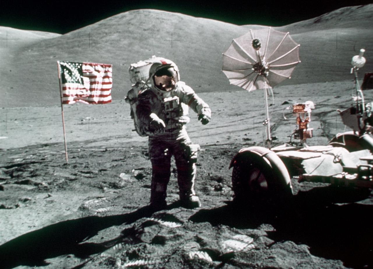 Astronaut on lunar surface; US flag behind; lunar rover beside