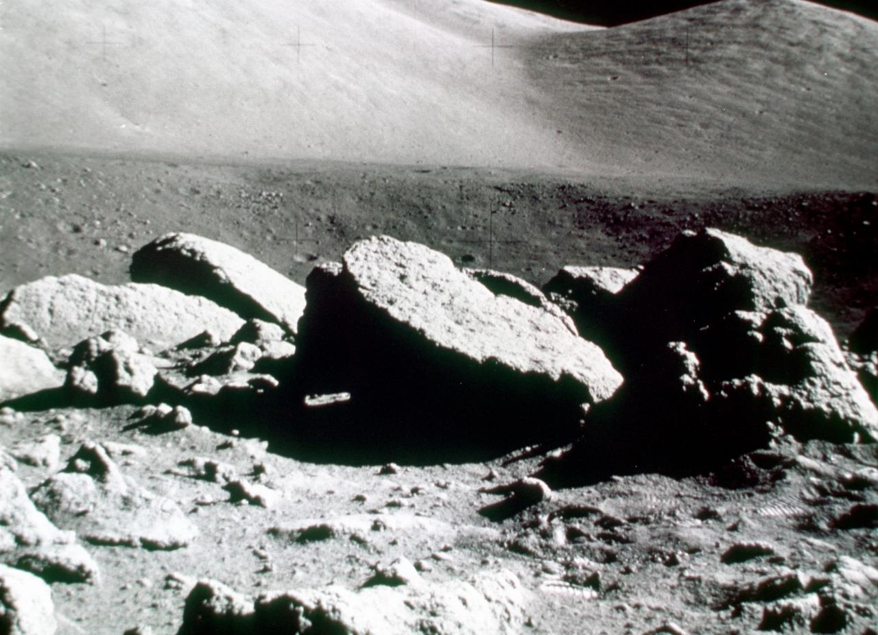 Lunar rocks in foreground, sloping ground with craters behind