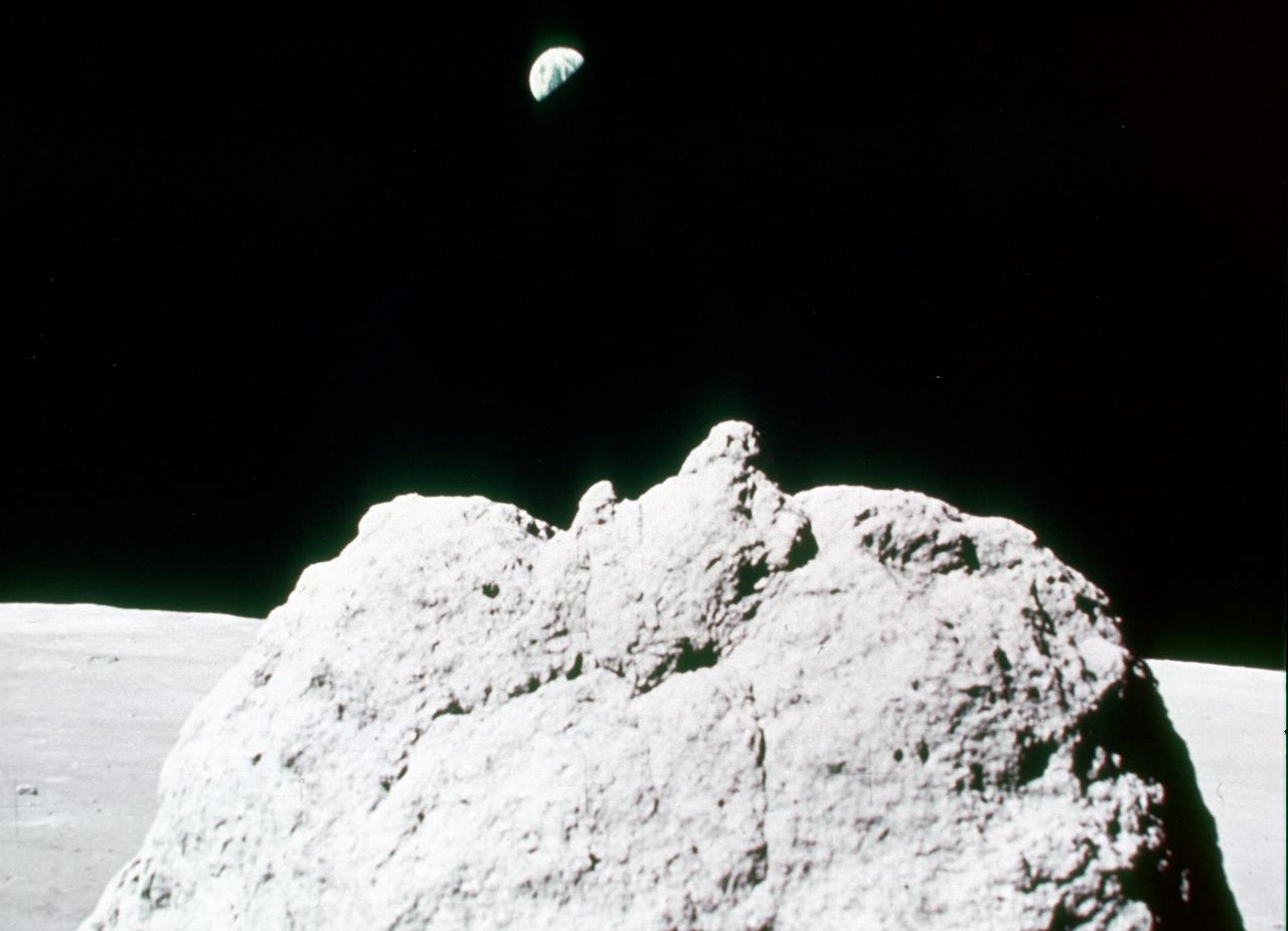 Distant half-earth above lunar rock in foreground