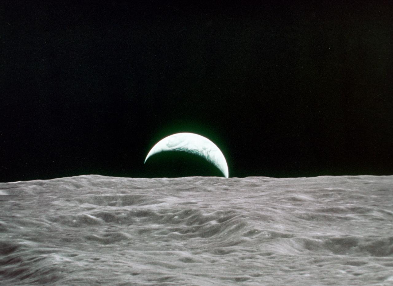 Crescent earth rising above moon's surface