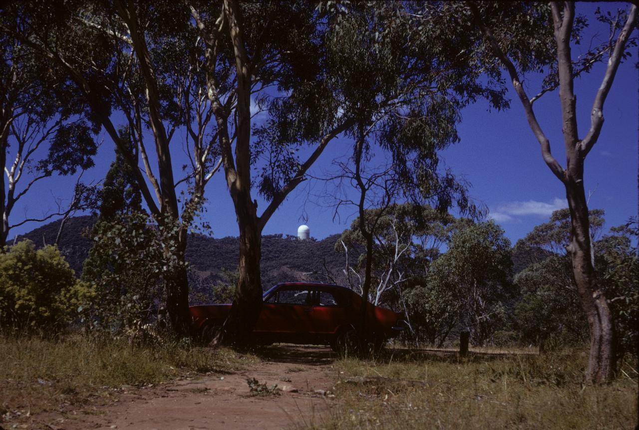 Car under tree and astronomical observatory dome on distant mountain