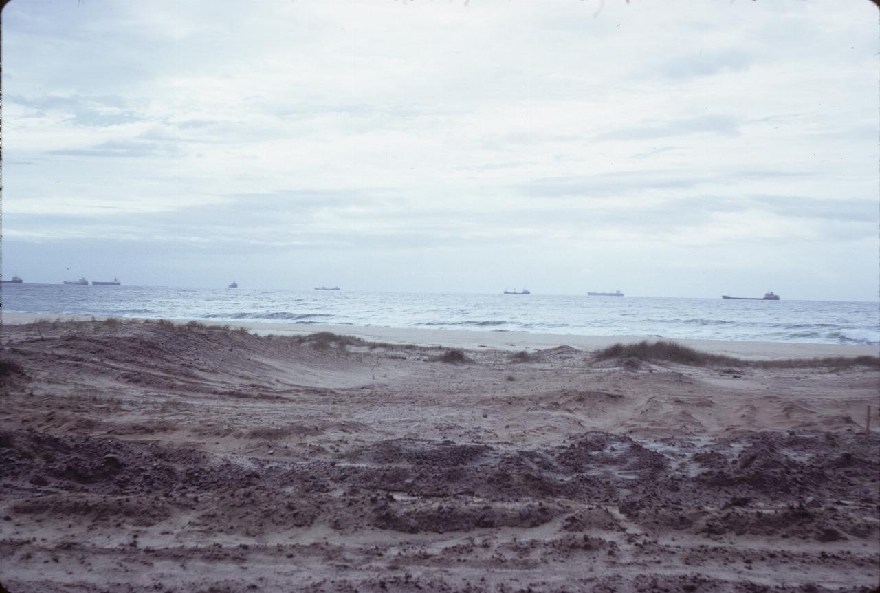 Ships sitting off the coast beyond a sandy beach