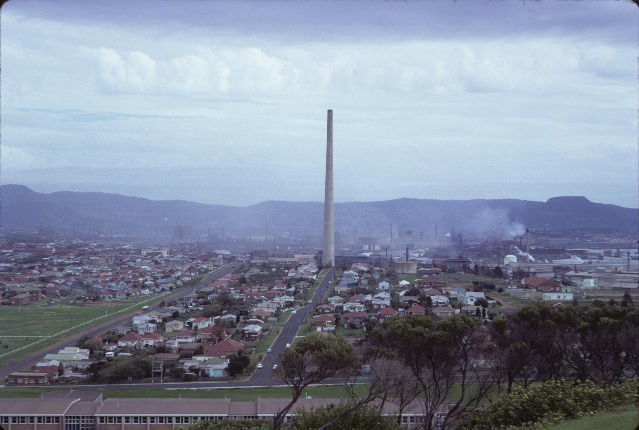 View over homes, very tall chimney, iron works and towards mountains, including Mt. Keira