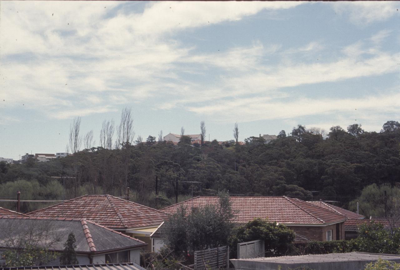 View across rooftops to tree covered hill with buildings at top