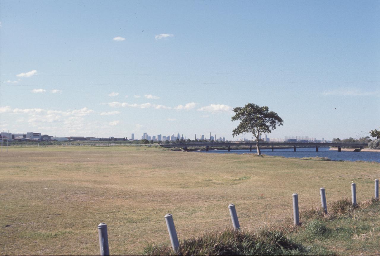 Brown grassy field on edge of canal; city skyline in the distance