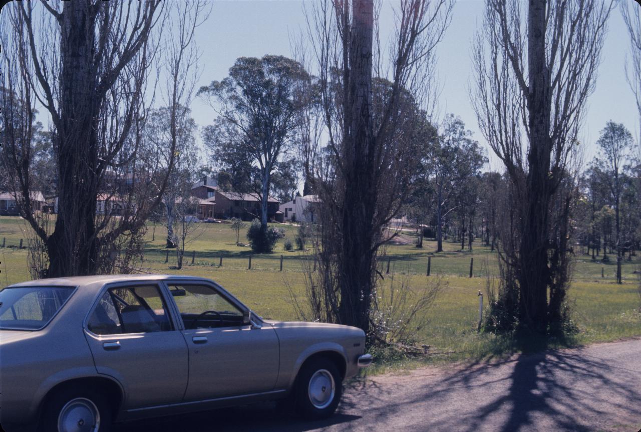 Car parked on side of road, with paddocks and house beyond