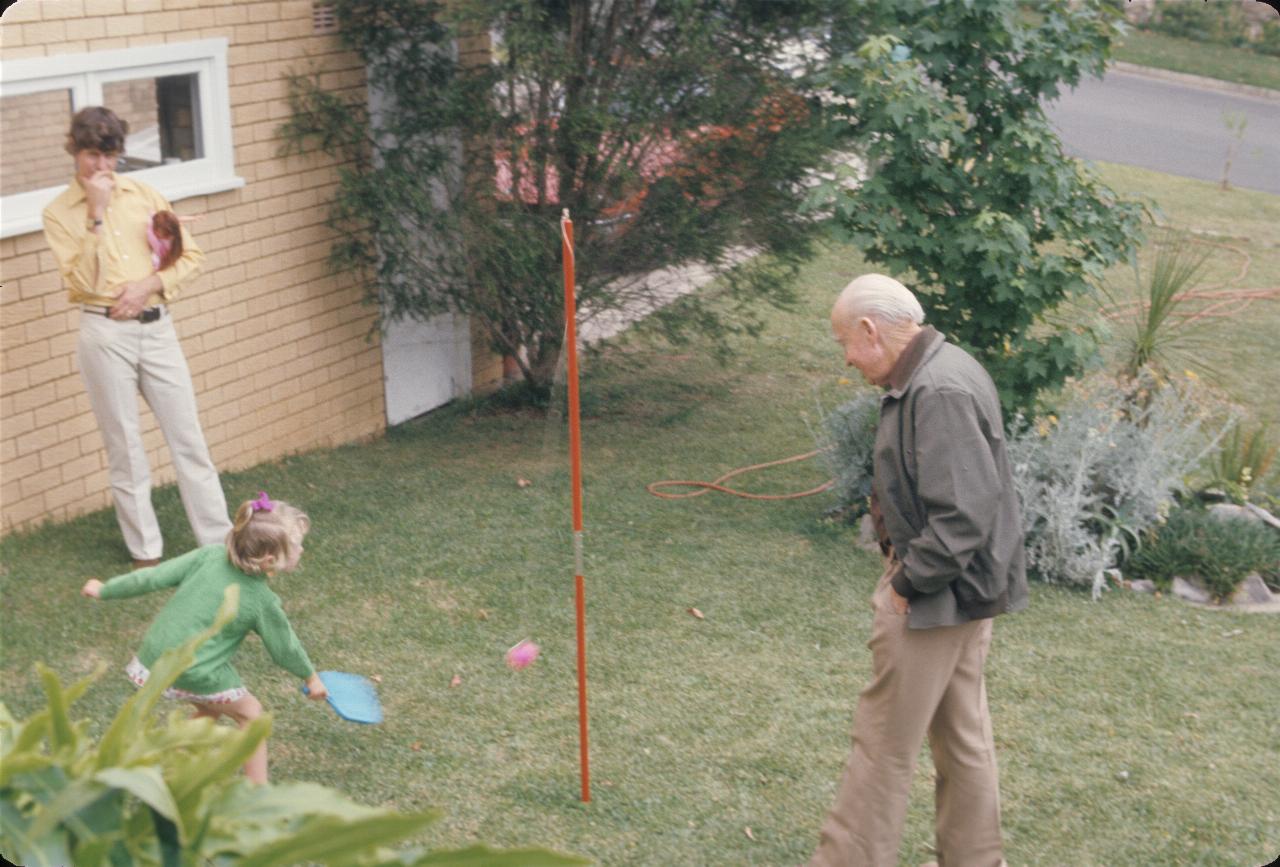 Father and grandfather watching little girl play tether tennis