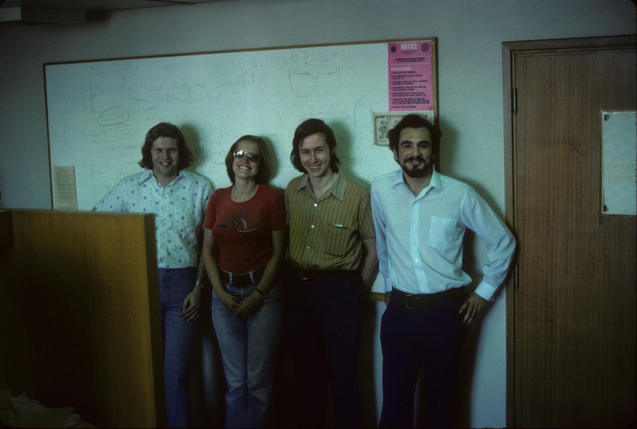 Four people standing against the wall inside