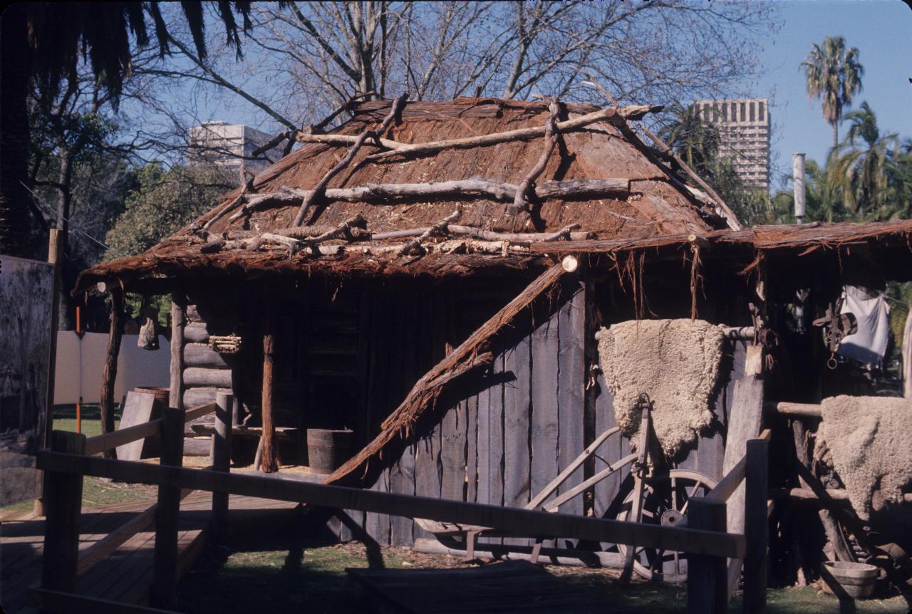 Crude log hut with bark roof and farm implements