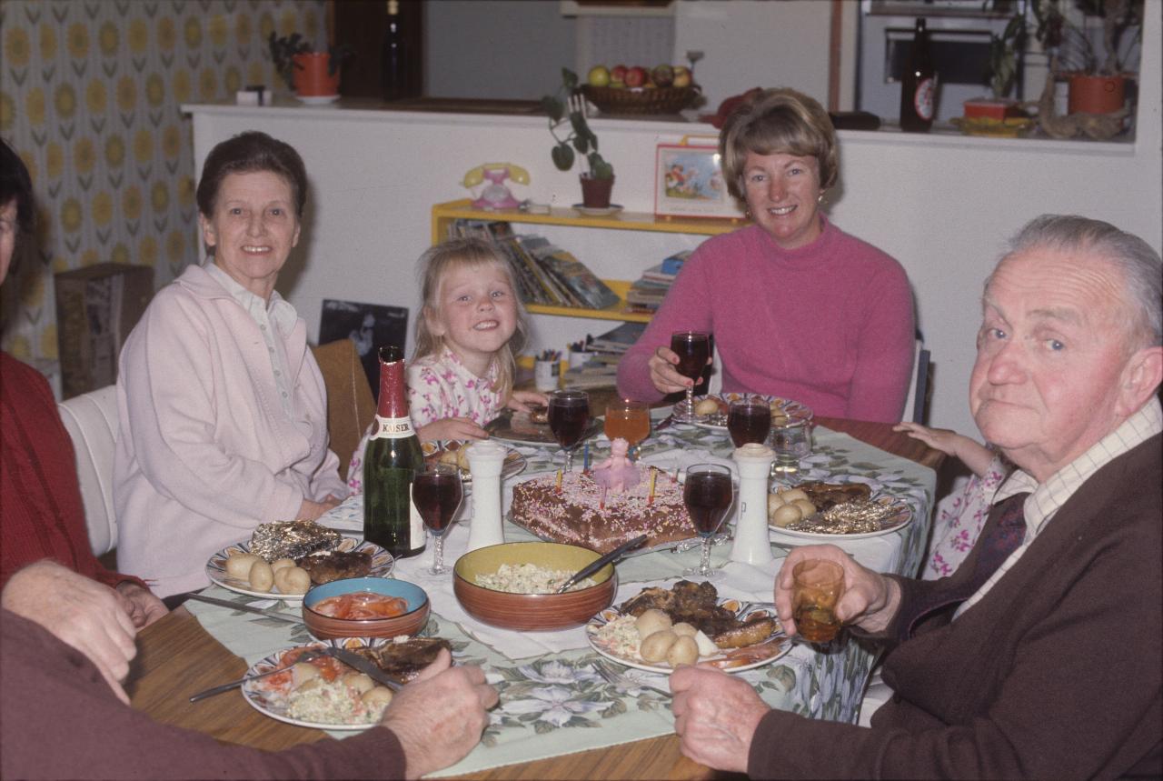 Adults and children sitting around dining table, with cake in middle