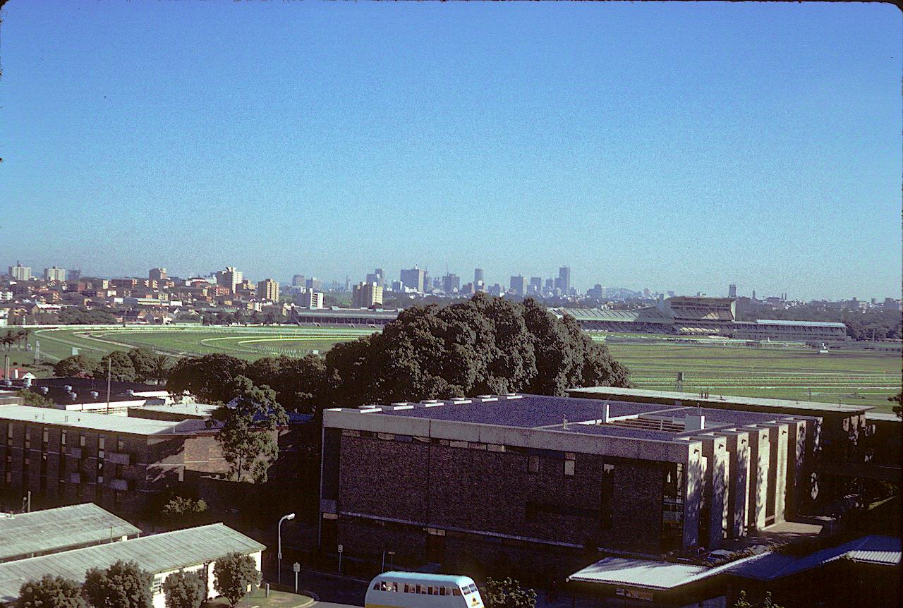 Brick buildings, green area on racecourse and city skyline in the distance