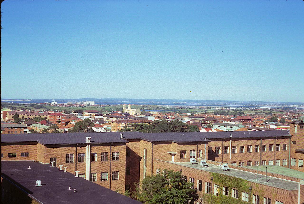 Brick building, houses and apartments beyond to bay and distant tree covered hills