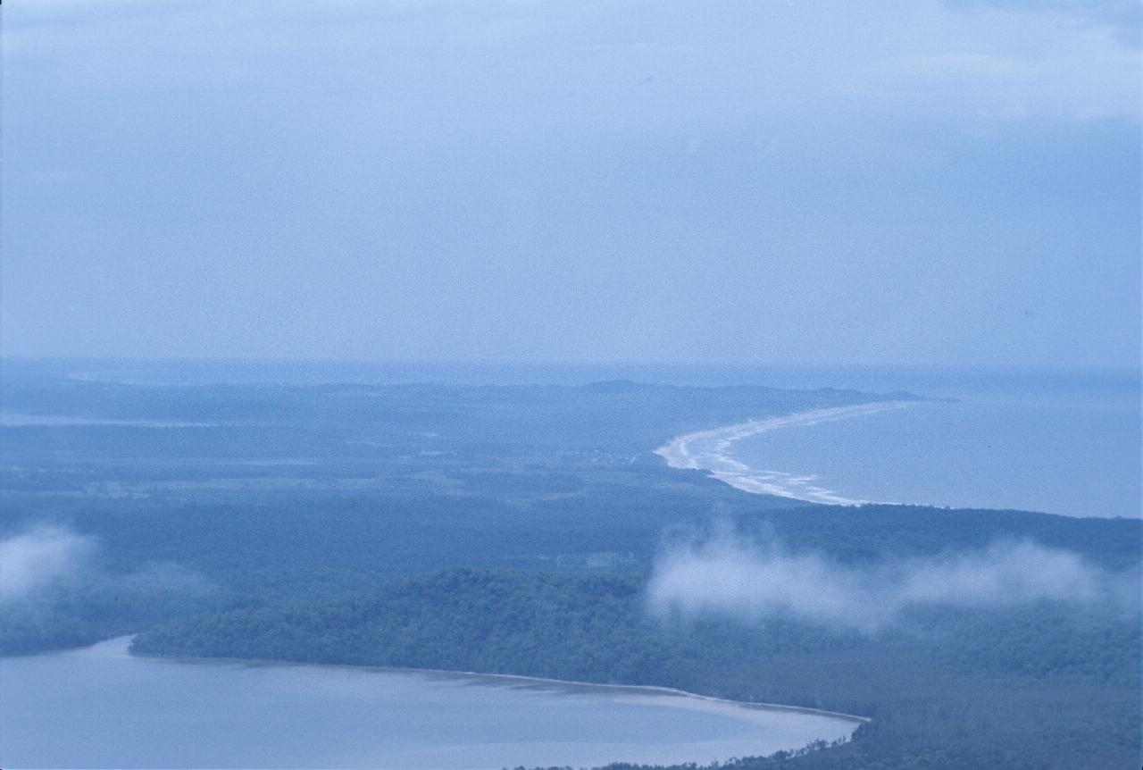 View along coast with sandy beach, breaking surf; distant haedland and nearby lake